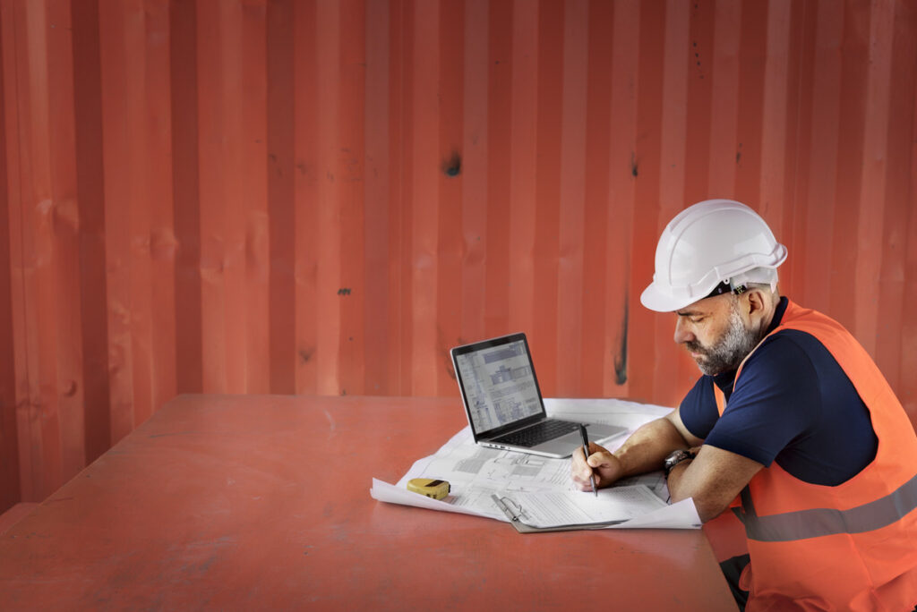 A construction superintendent is submitting jobsite work details via his laptop